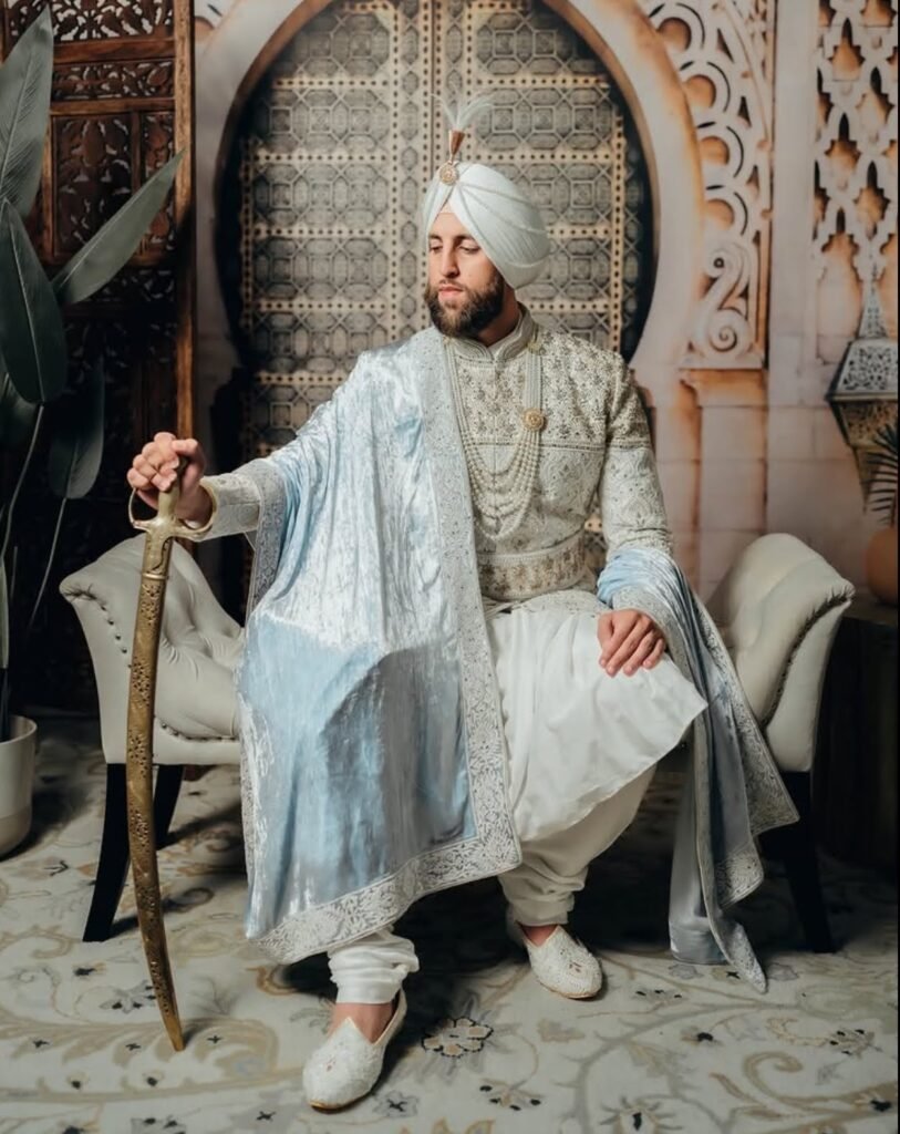 Groom wearing white embroidered sherwani with anarkali kurta, shawl, necklace and a sword