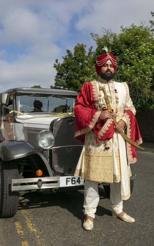 Groom in Maharaja Sherwani with red shawl and red turban with a nice vintage car in background
