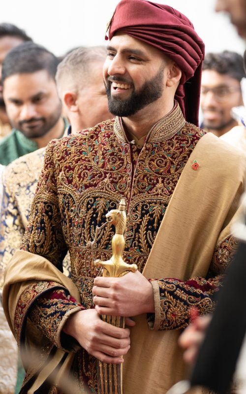 Groom in rich red embroidered maharaja sherwani with shawl and sword